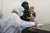 A woman holding a baby on her him looks on while a woman in white coat makes some notes in a book.