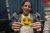 A woman holds up a yellow cardboard cutout of a smiling emoji with red heart-shaped eyes.