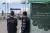 Two men look at a border crossing, where loaded trucks are waiting.