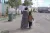 A woman carrying a large box on her shoulder, walks next to her daughter who is carrying a while bag.