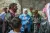 A woman wearing a blue UNICEF coat speaks members of the community who are standing around her.