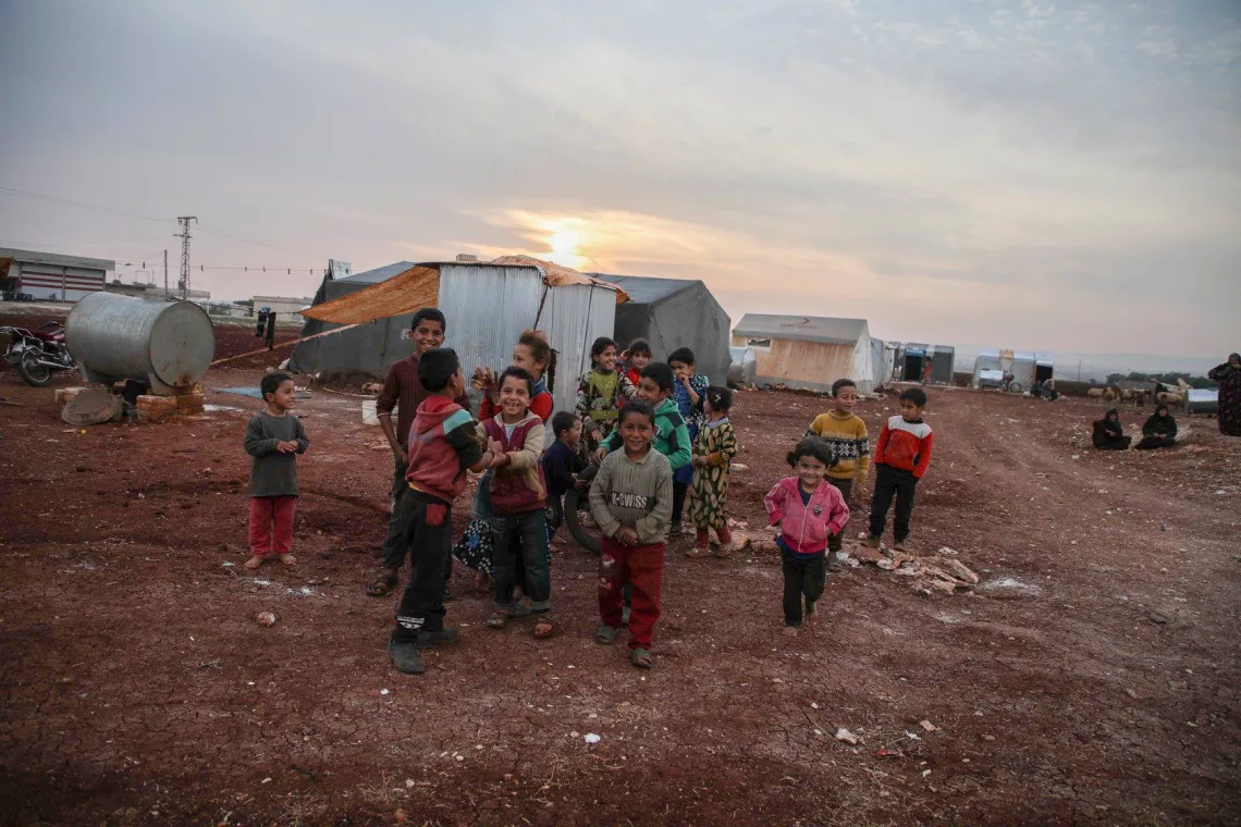 Children play in front of tents in a camp 