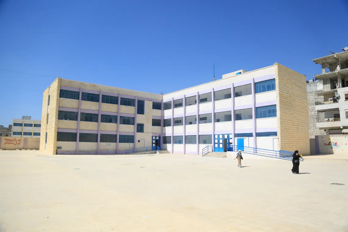 Three-story school building with 2 wings connected at a right angle. The building's entrance is painted UNICEF blue.