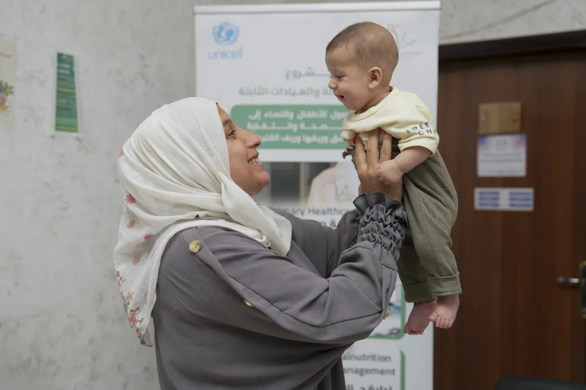 A woman lifts her baby boy into the air with joy.