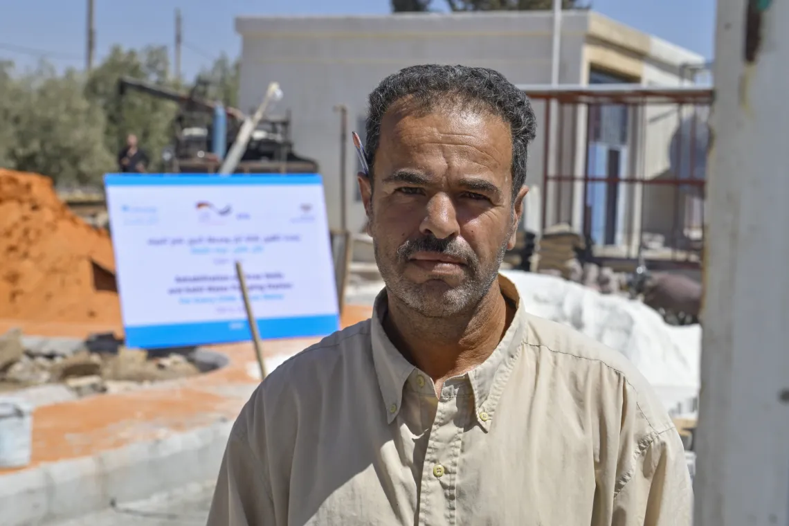 Portrait of man standing on street, with a large sign at the back with UNICEF and other logos on it.