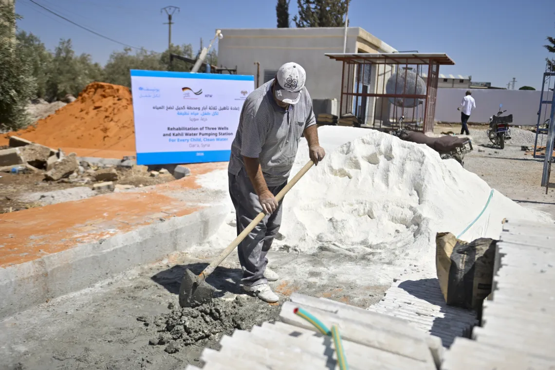 A man with a shovel smooths out freshly mixed concrete, in front of large white heap on a road.
