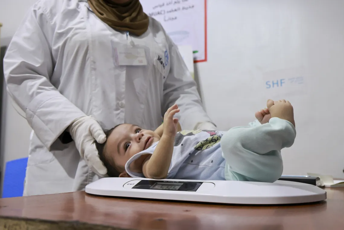 A baby looks to the side while lying on scale in an examination room.