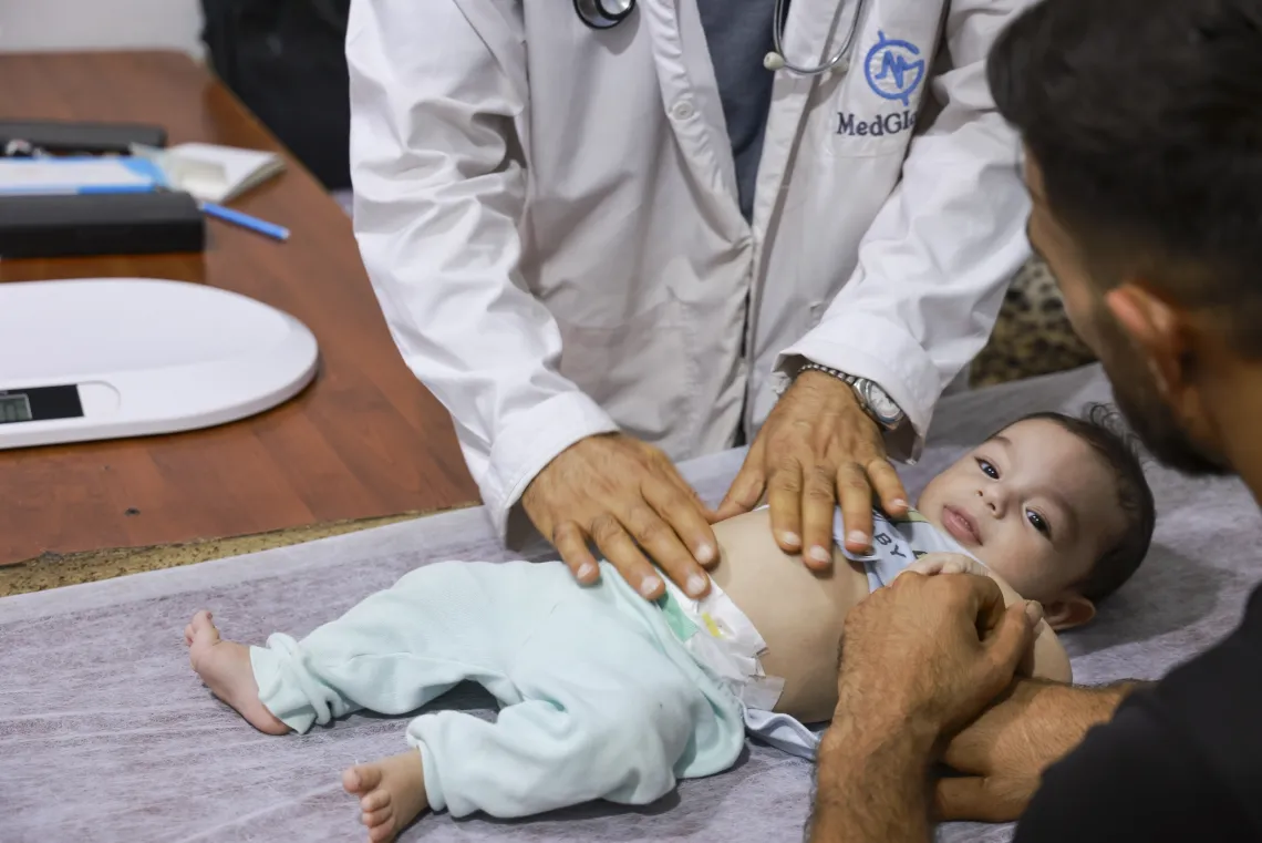 A baby lying on his back is being examined by a doctor wearing a white coat.