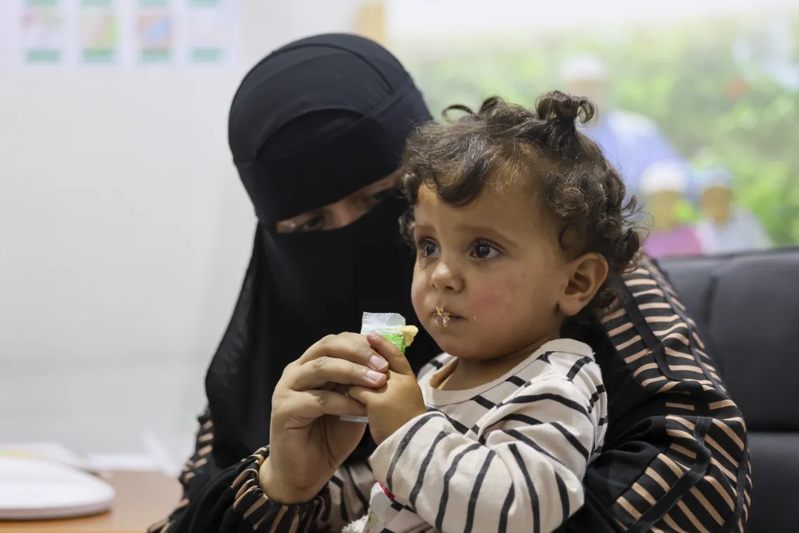 A woman feeds a little girl a supplement from a sachet.