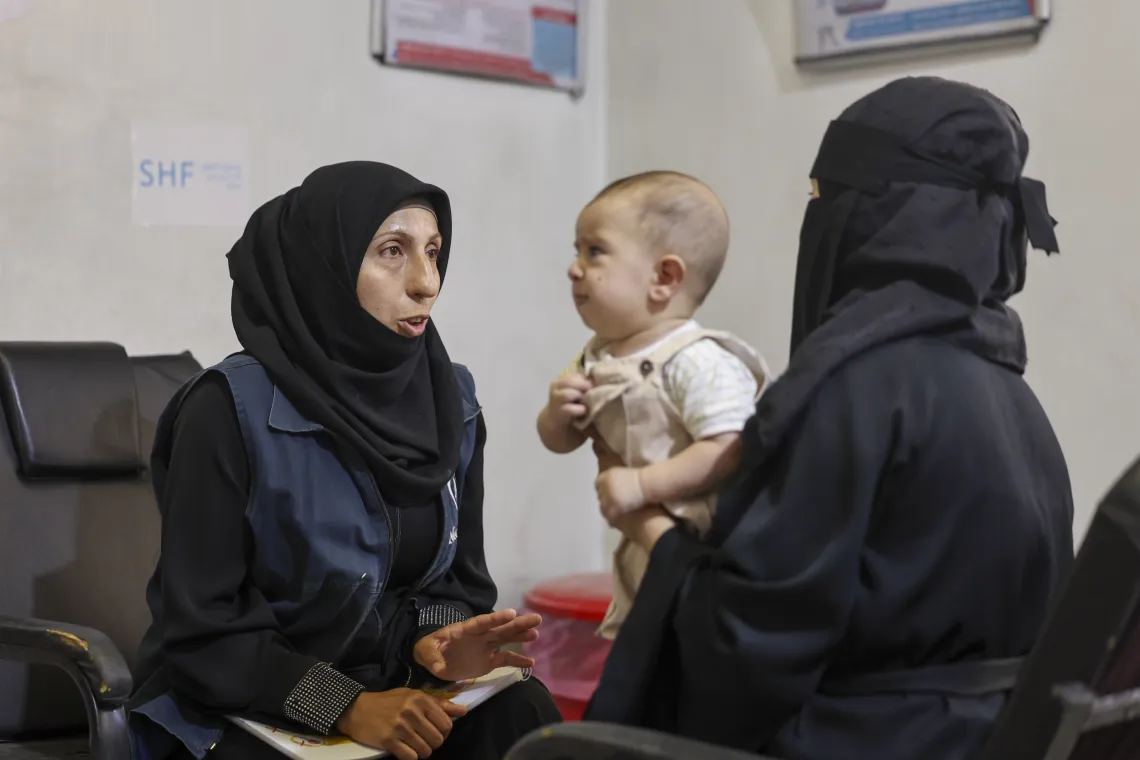 A woman wearing black speaks to another woman who is holding a baby.