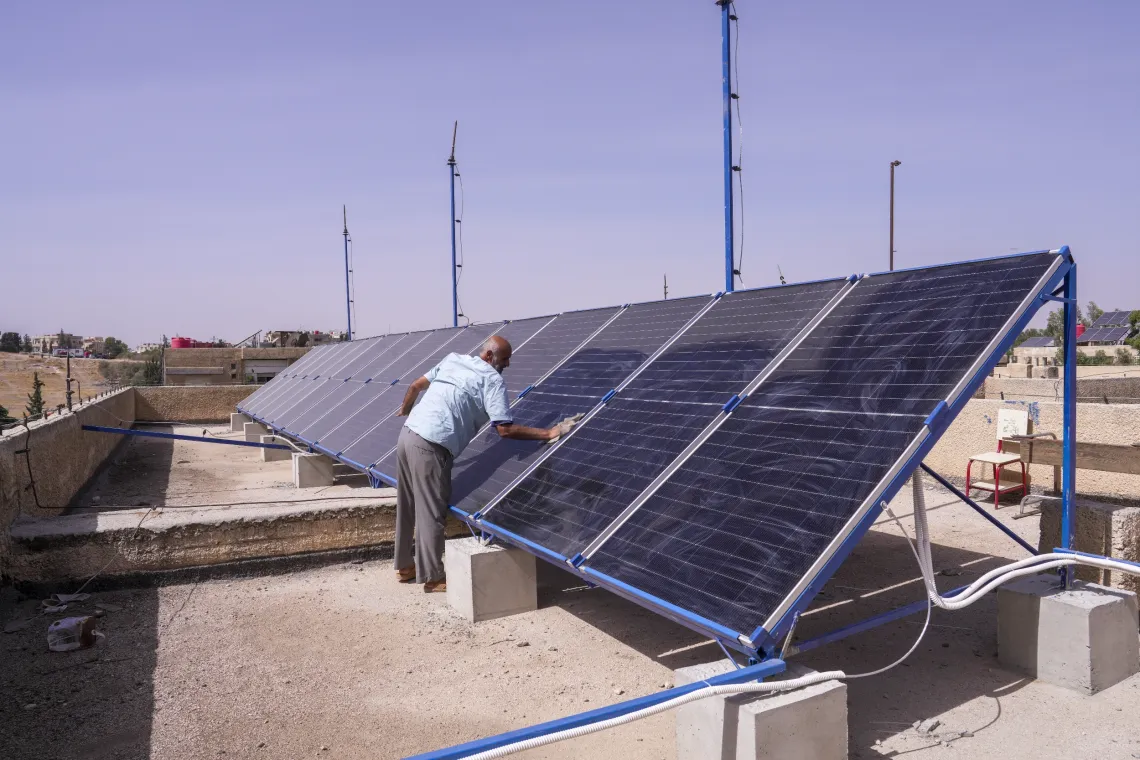 Solar panels installed in a row, with a man cleaning one of them.