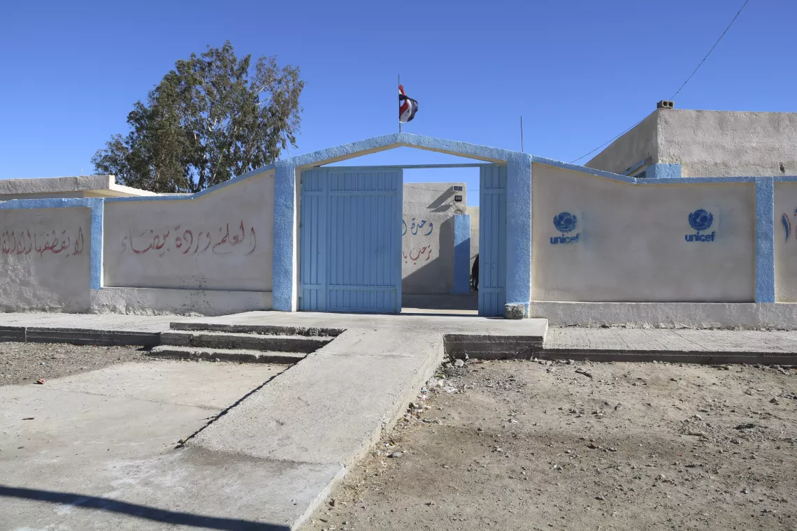 A bright white wall with big blue gates at the entrance of a school