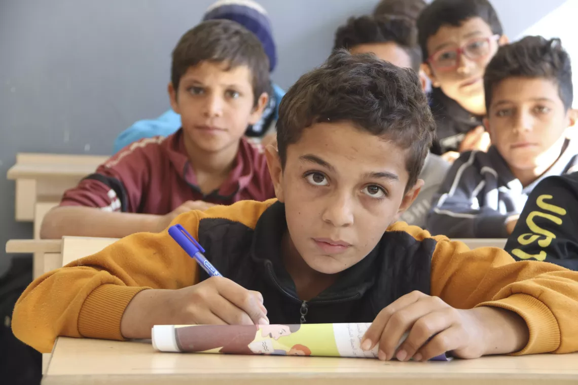 A boy looks up from writing in his book in class.