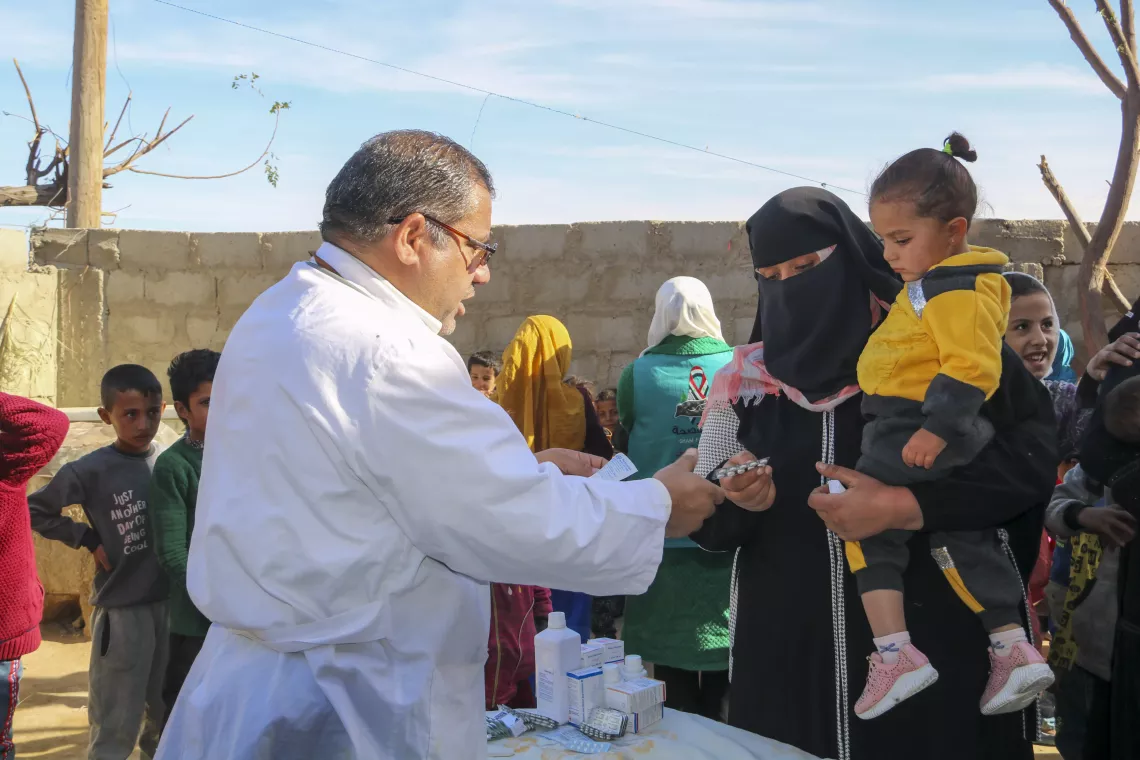 A doctor hands medicine to a mother who carries her little girl on her hip.