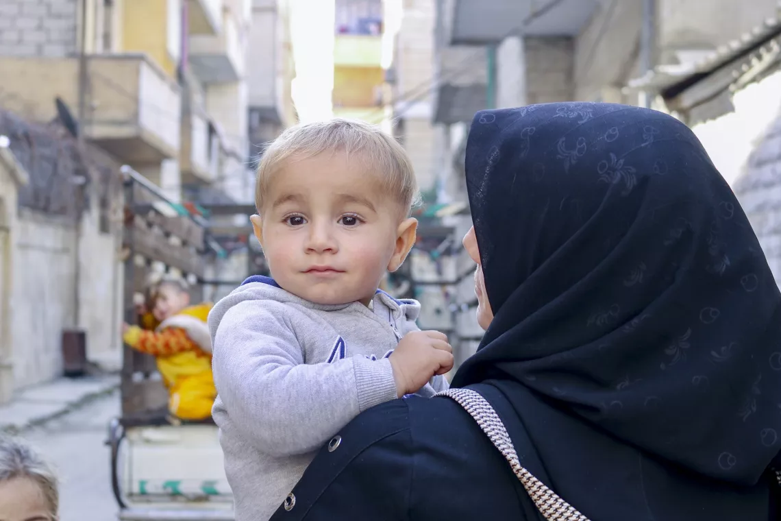 A little boy looks over his mother's shoulder who is carrying them.