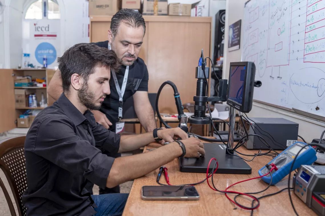Elia, 17, repairs a mobile phone under the guidance of his course trainer at a UNICEF-supported youth-friendly space in Jaramana, Rural Damascus.