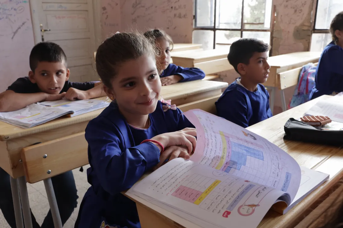 A girl smiles as she turns the page in her textbook on the desk in front of her.