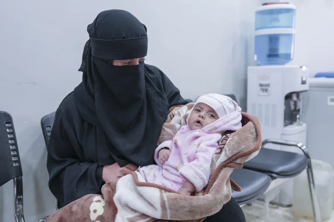 A woman looks down at her baby in her lap.