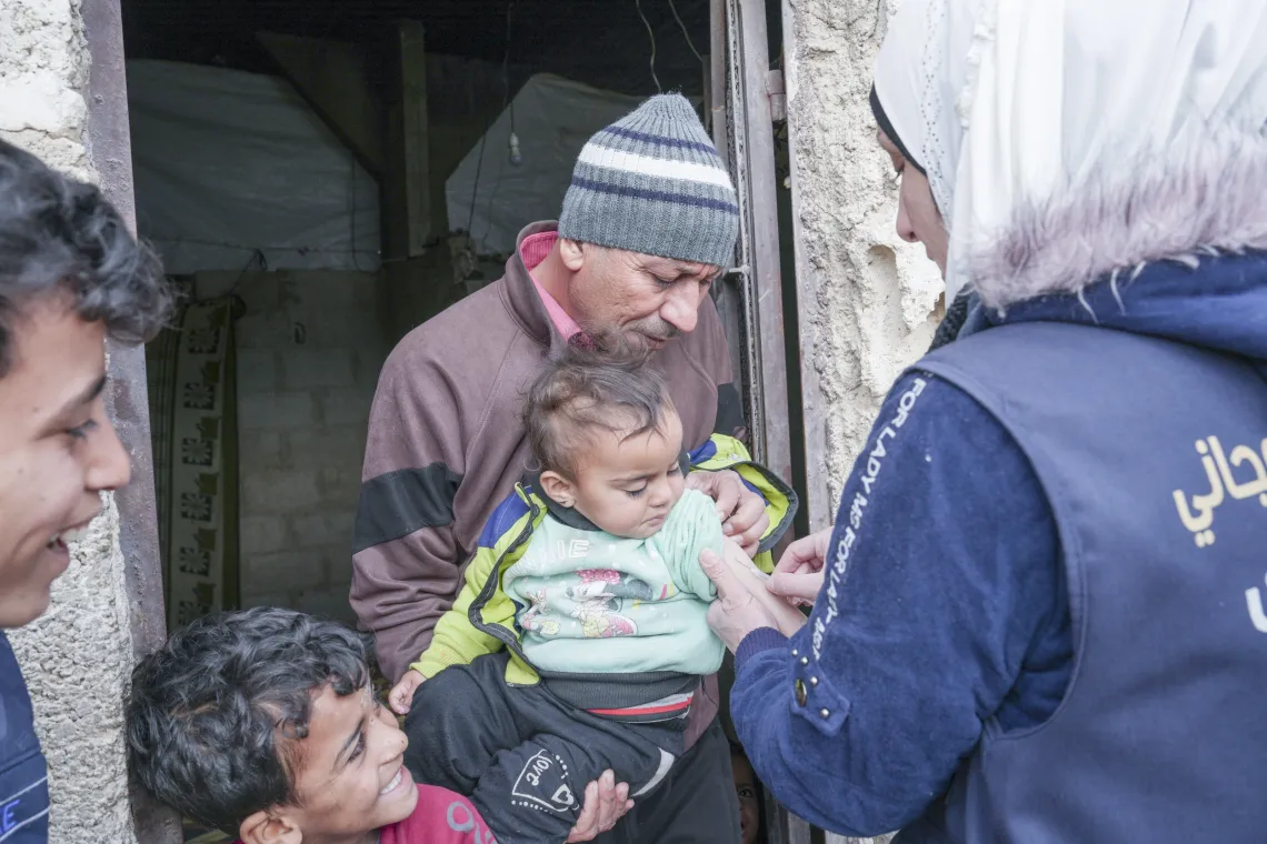 A man holds his grandchild, while a health worker prepares a vaccine.