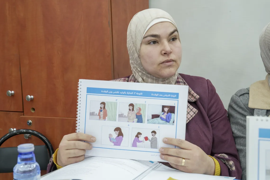 A woman holds a manual with pictures of pregnant women and mothers with babies, and text captions..