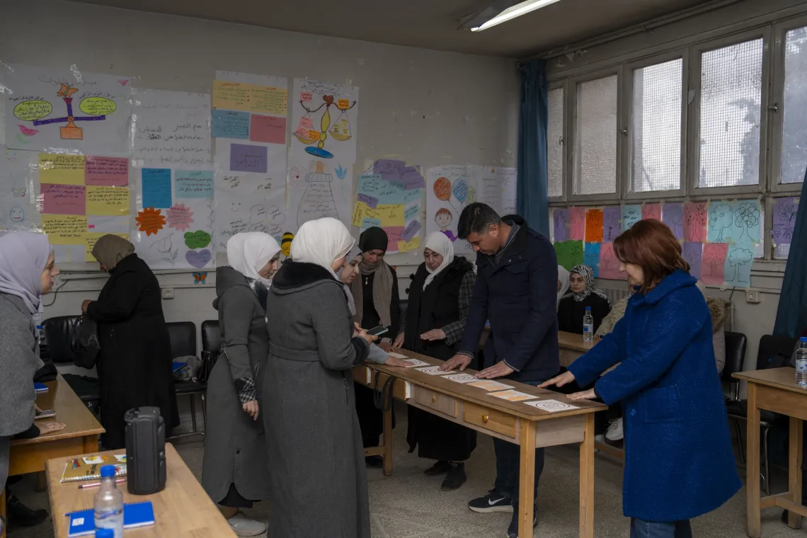 Teachers take part in a group activity, standing around a long narrow table, sorting items on it.