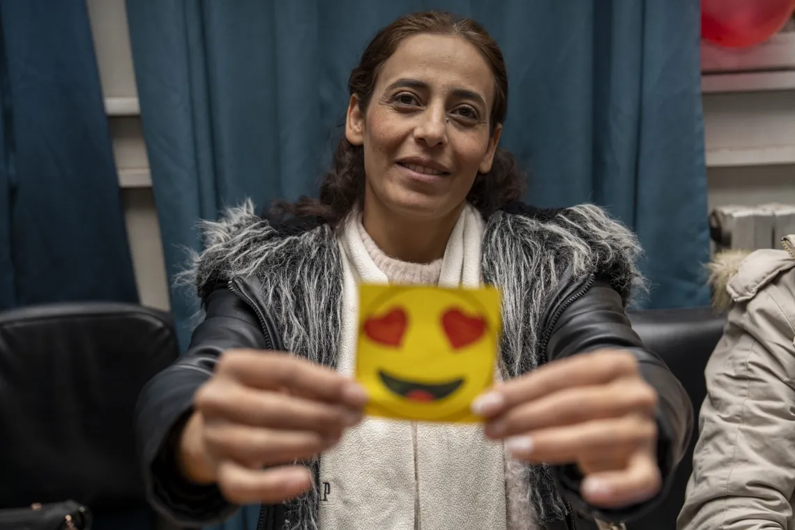 A woman holds up a yellow cardboard cutout of a smiling emoji with red heart-shaped eyes.