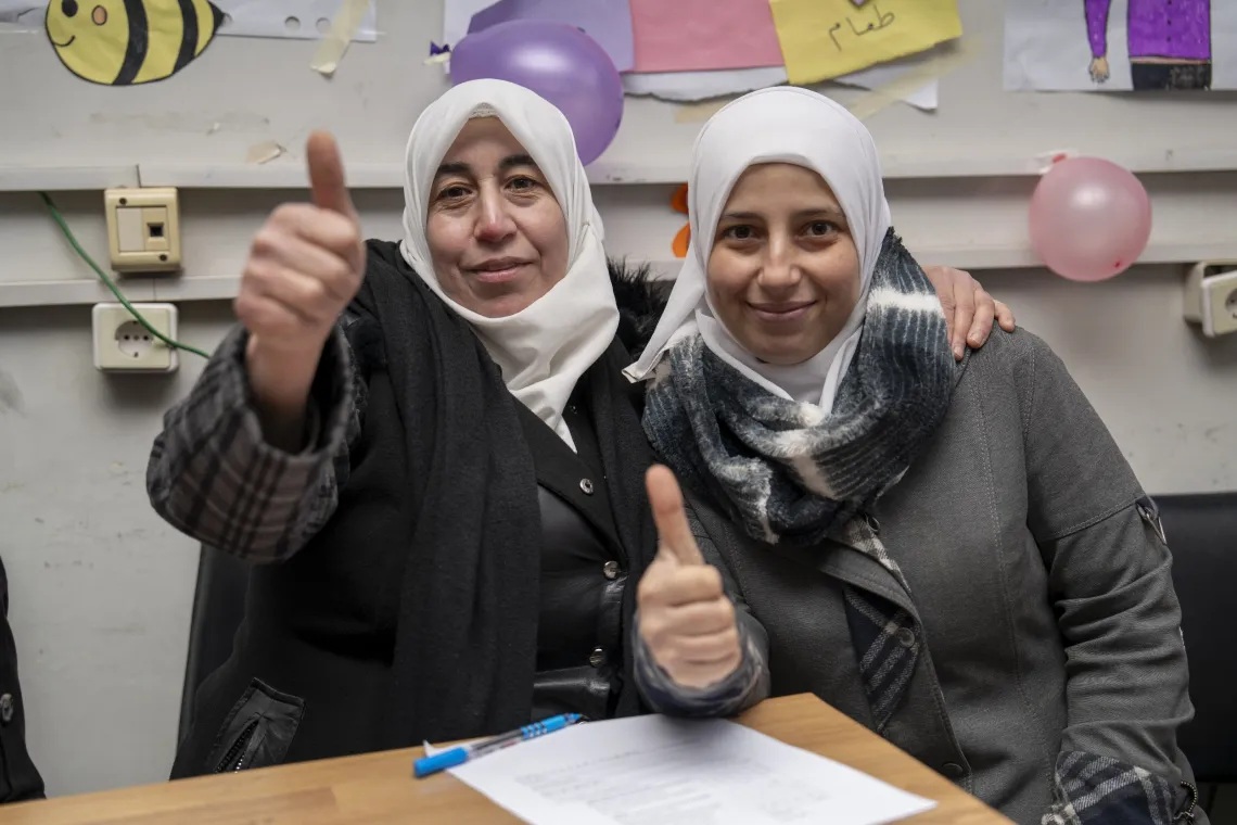 Two women sitting next to each other, smile while both give a thumbs up.