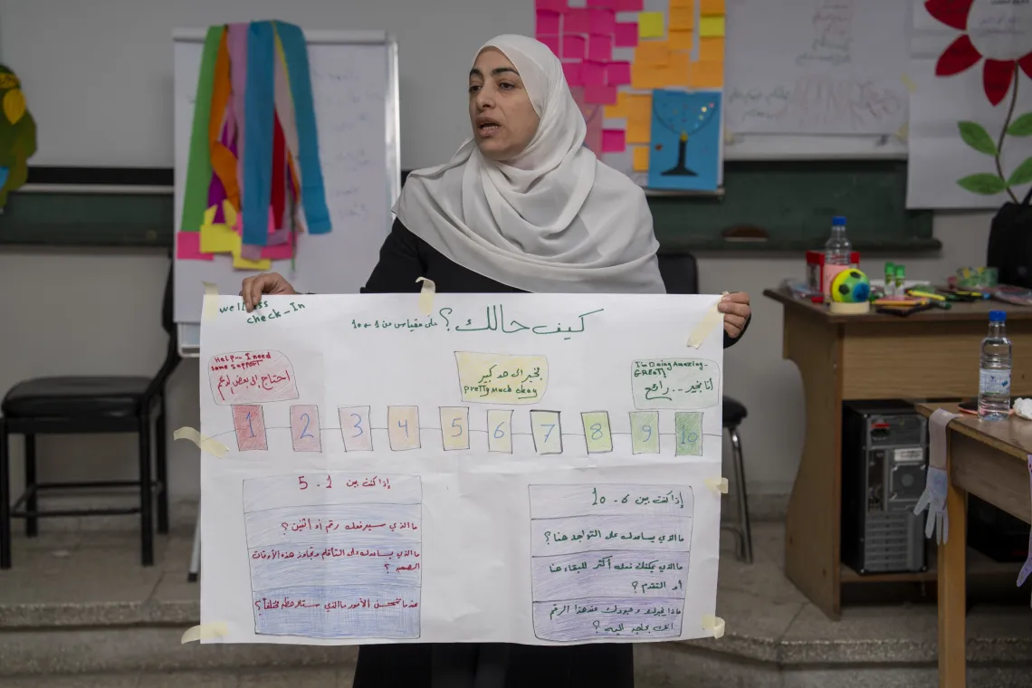 A woman holds up a large poster with a colourful chart and handwritten Arabic text.