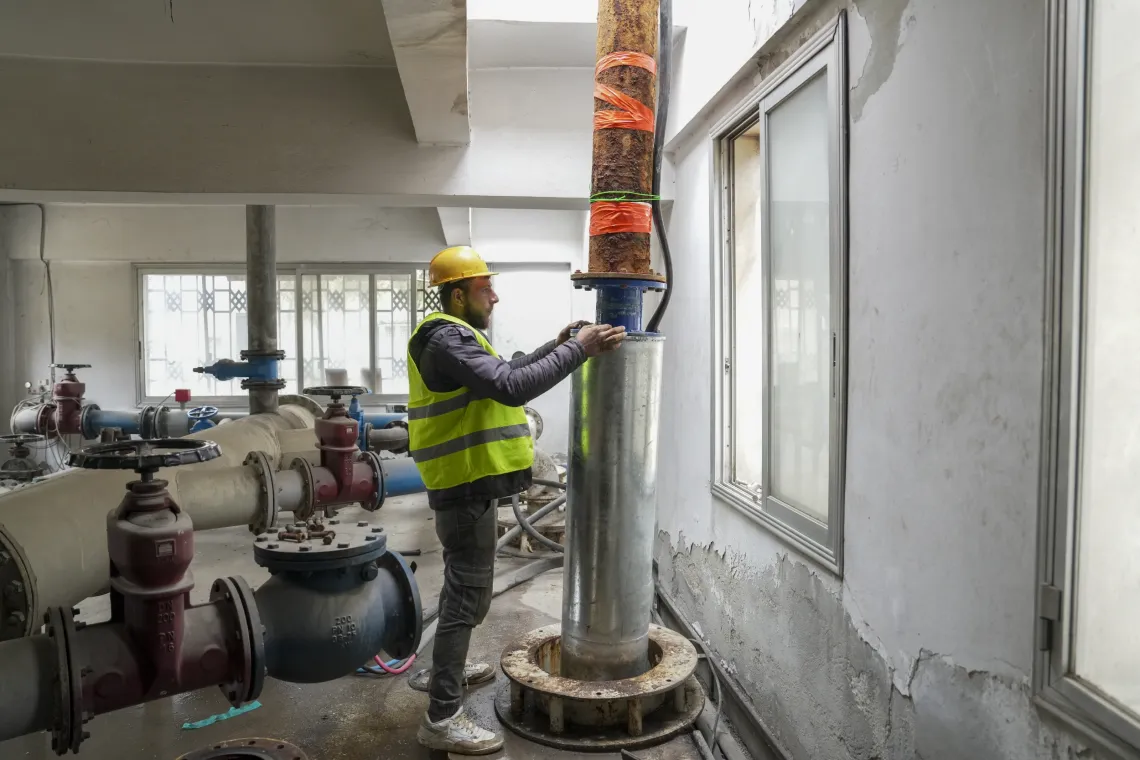 A technician lowers carefully a submersible pump into a water storage tank.