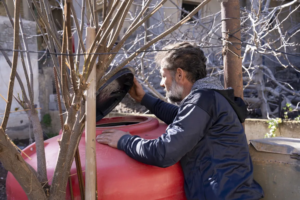 A man lifts the lid on a large red water tank to have a look inside.