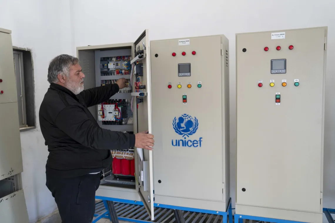 A man inspects a control panel inside a large box, next to similar closed boxes with UNICEF logos on.