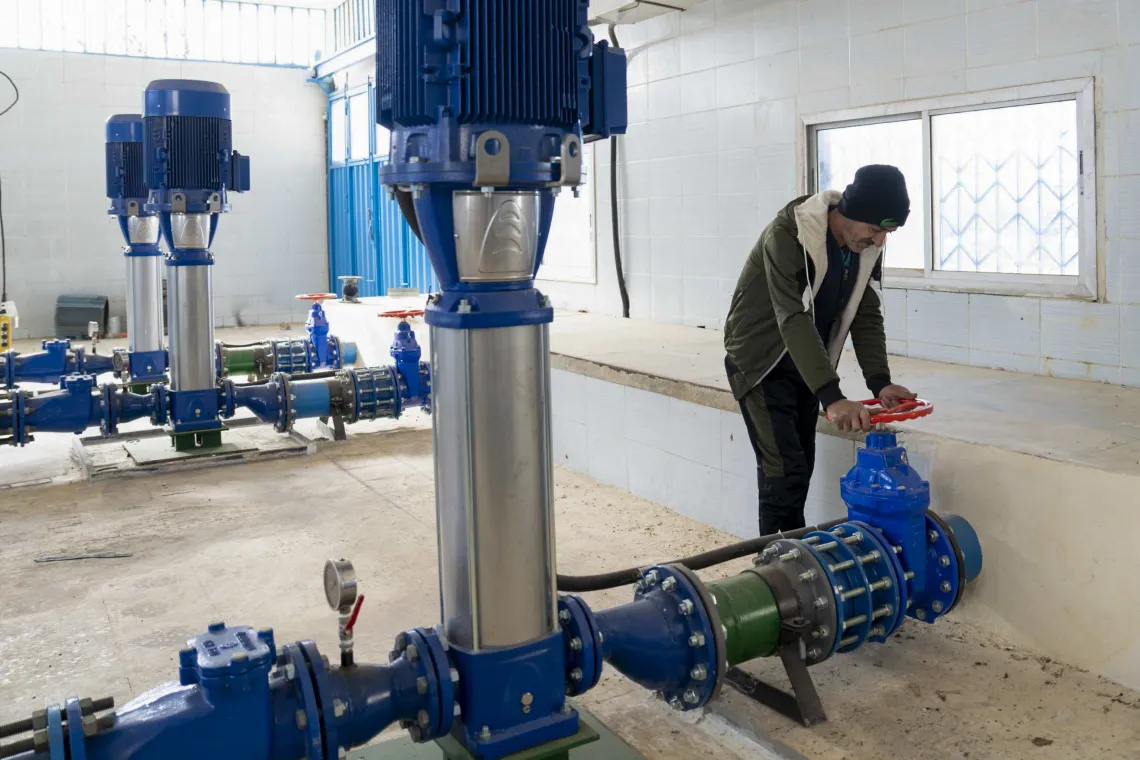 A man turns a large valve attached to pipes inside a pump station.