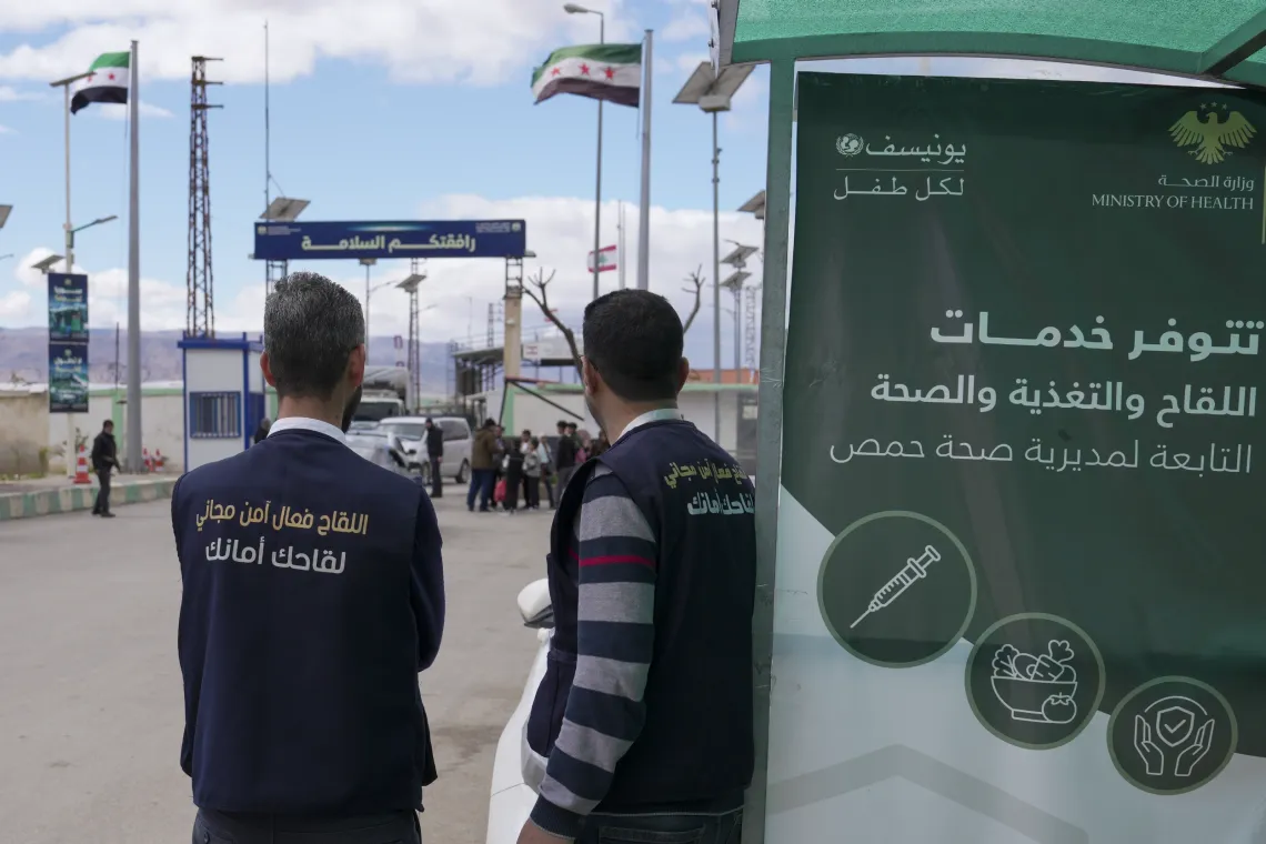 Two men look at a border crossing, where loaded trucks are waiting.