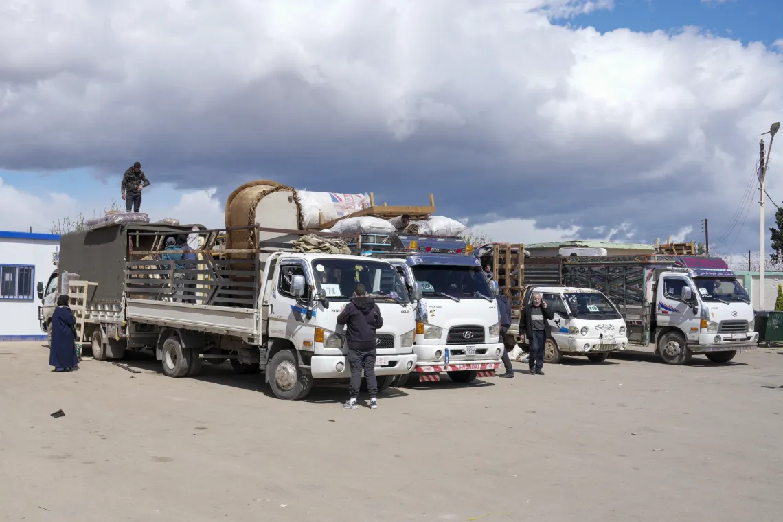 Trucks and cars loaded with belongings are parked in a row.