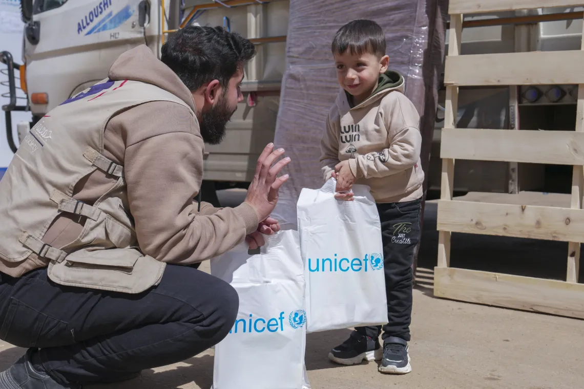 A young boy holds a white bag with a UNICEF logo on it, while listening to a man explaining something to him.
