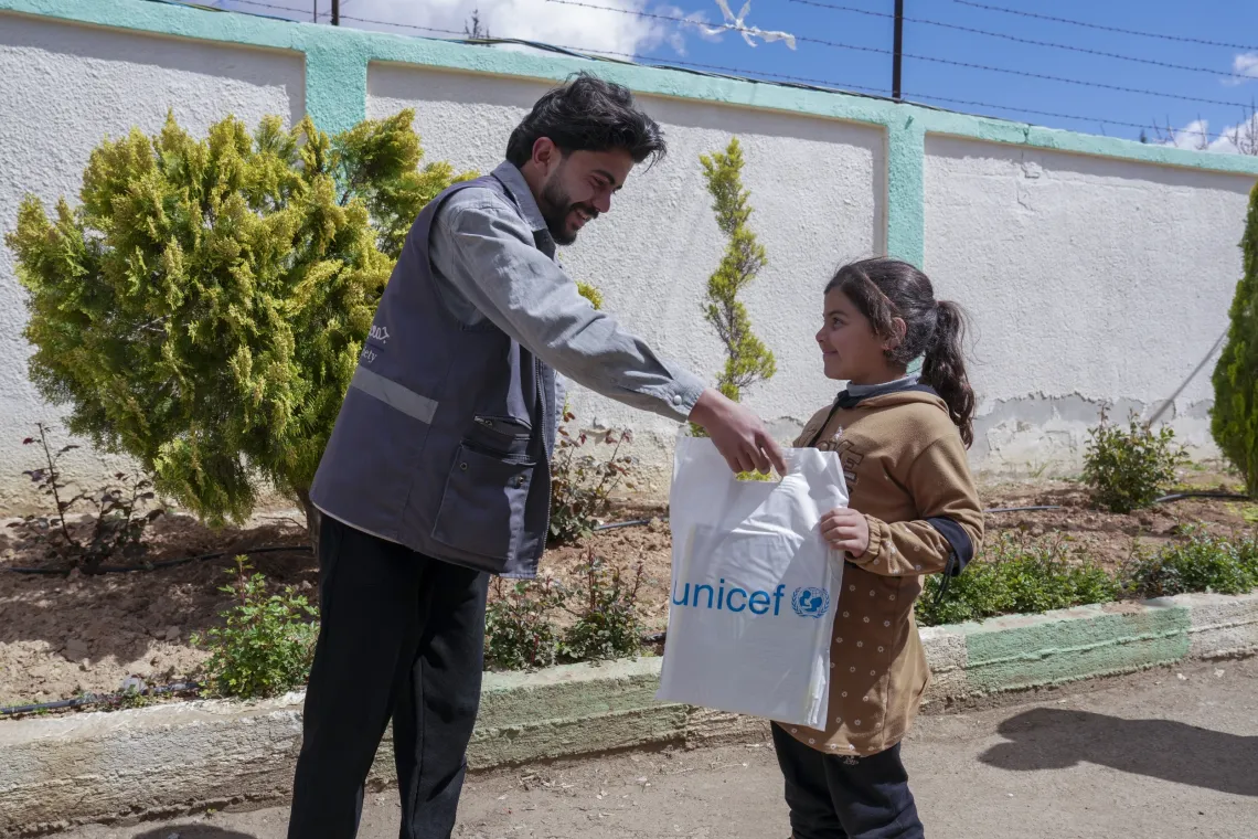 A young girl receives a bag with a UNICEF logo on it from a man.