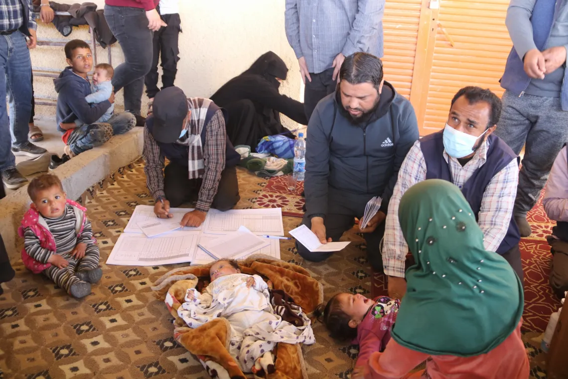 Three members of the vaccination team sit on a carpet, registering children.