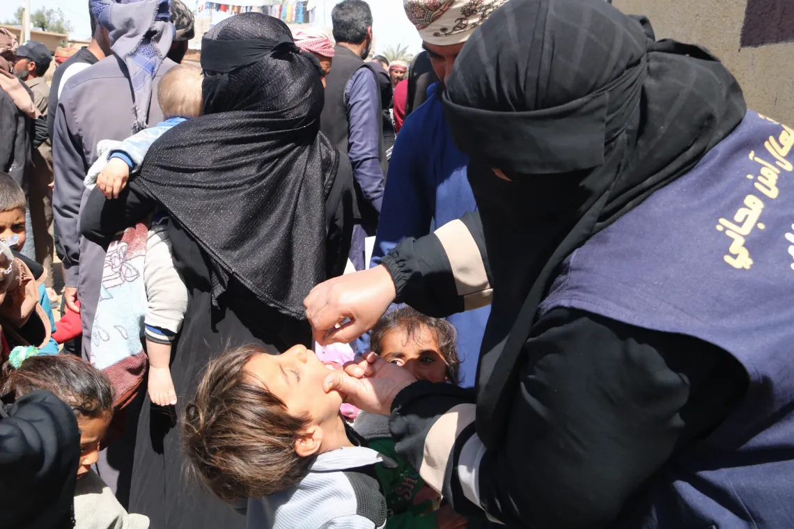 A vaccinator administers an oral vaccine to a child.