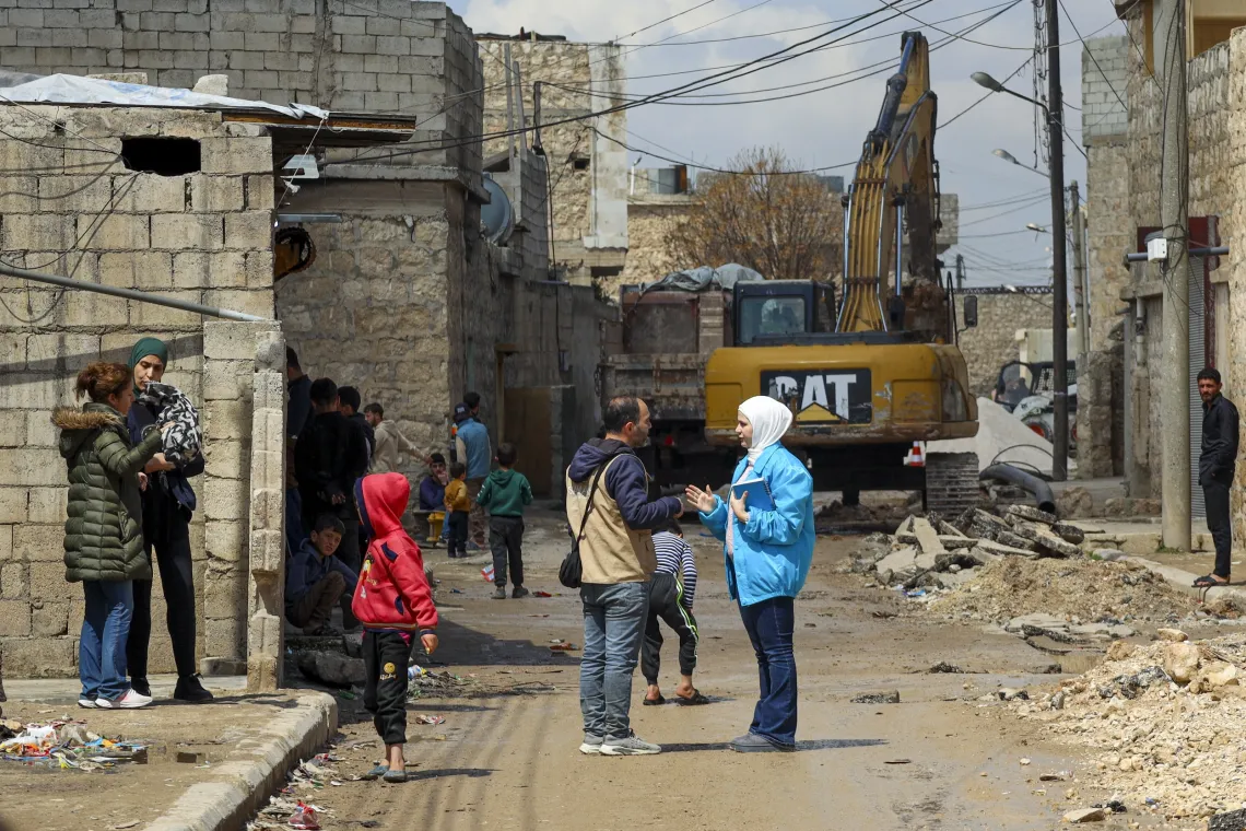 A woman wearing a blue UNICEF coat speaks members of the community on street with a large digging equipment in the distance.