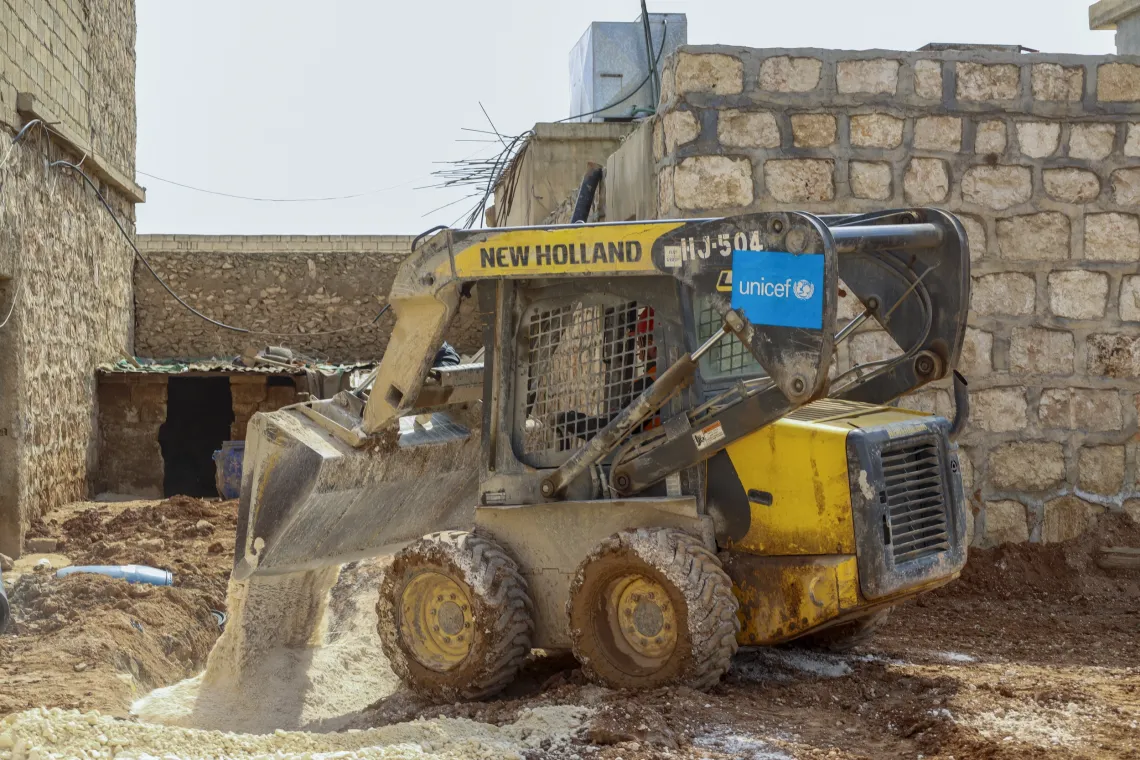 A small yellow bulldozer pushes dirt to fill a ditch.