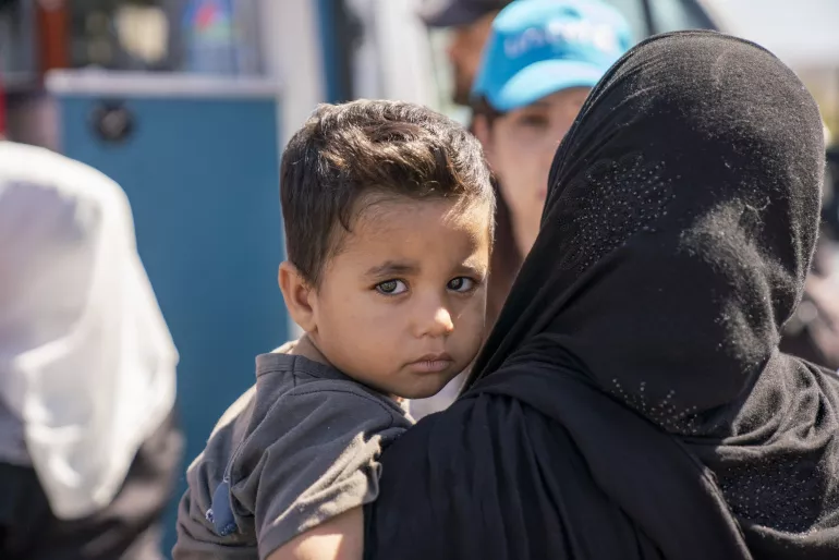 A tired looking little boy looks over his mother's shoulders.