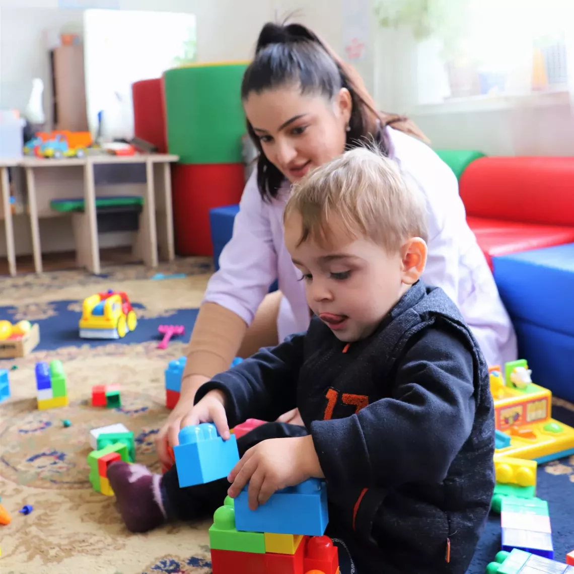 little toddler is building a tower out of lego blocks
