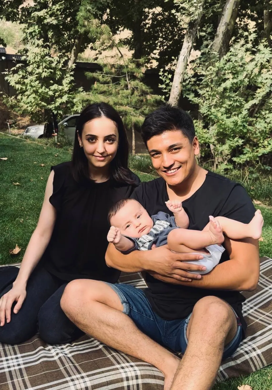 A mother, a father and a son sitting on the ground in the park