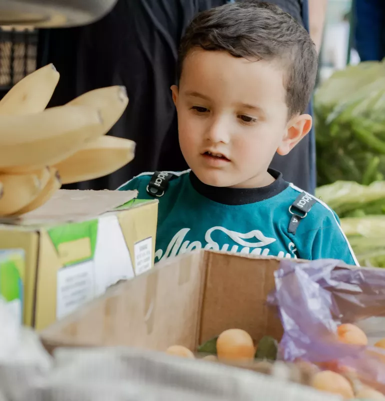 a little boy is looking at bananas in a local market