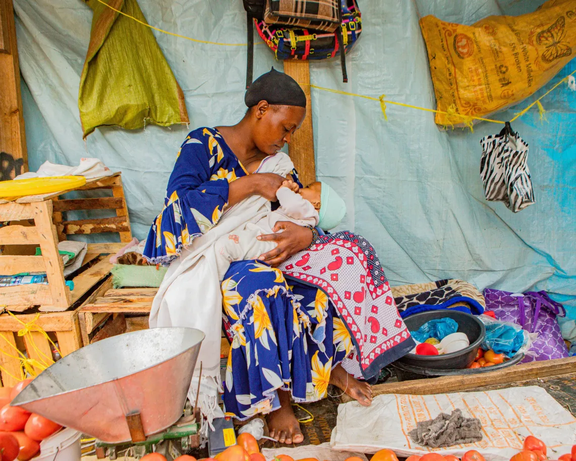 Salome breastfeeds one of her twins at her stall.