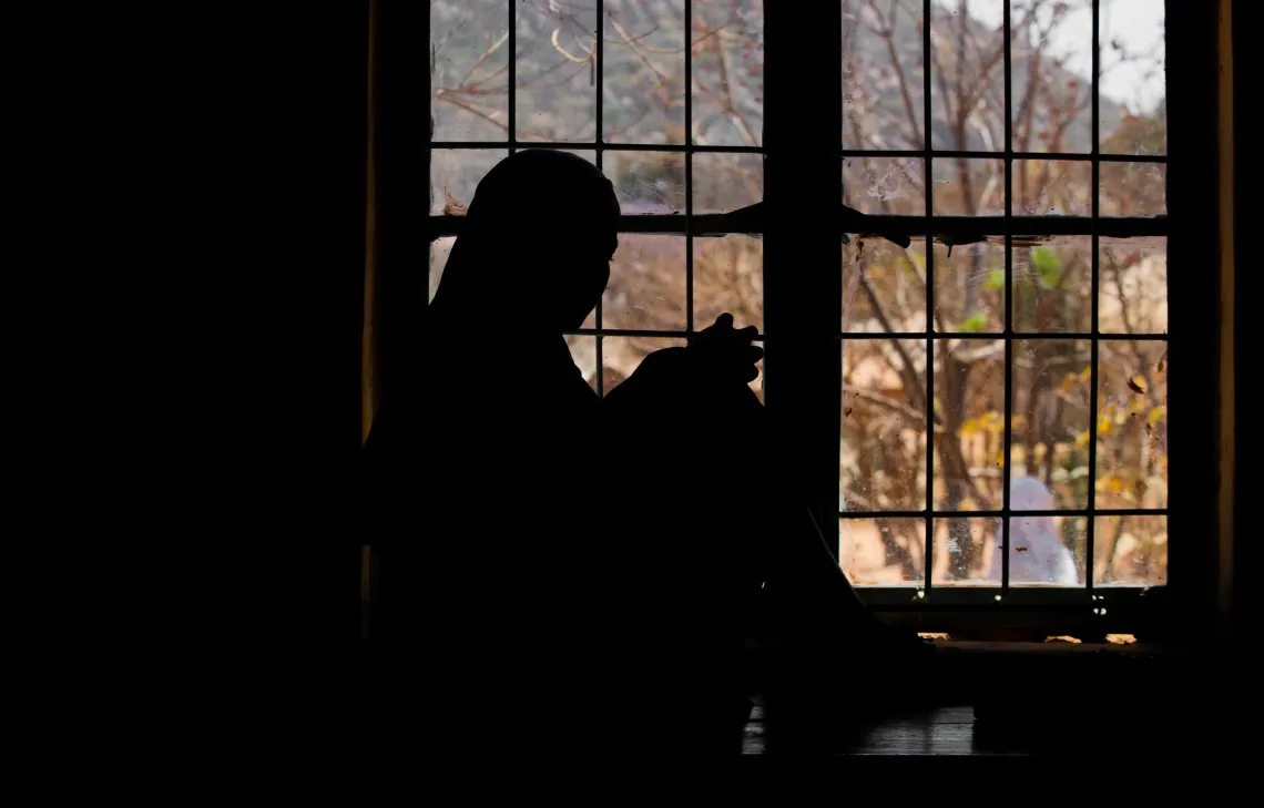 Silhouette of a girl sitting in the dark looking out the window 