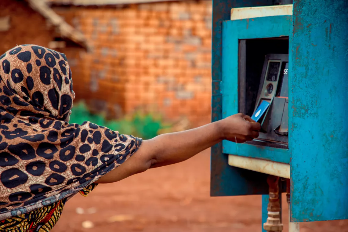 Ashura Samgao, Tausi's mother, uses a prepaid water card to access water at an AQtaps water point. 