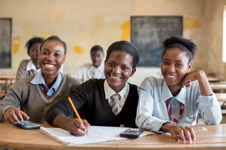 Adolescent girls, including one taking notes, smile during a class