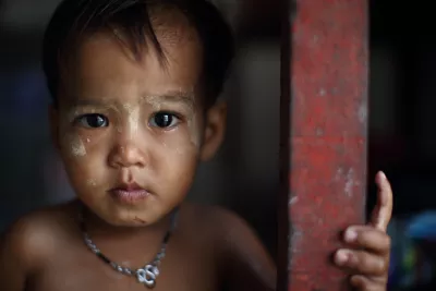 A young boy with a sad face looking out of his house.