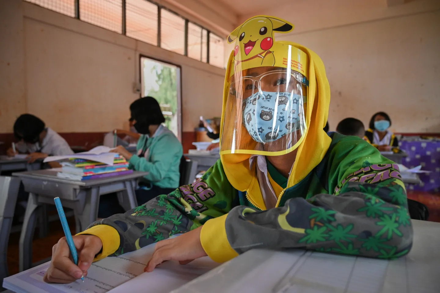 A student wearing a face shield is taking note in the classroom.